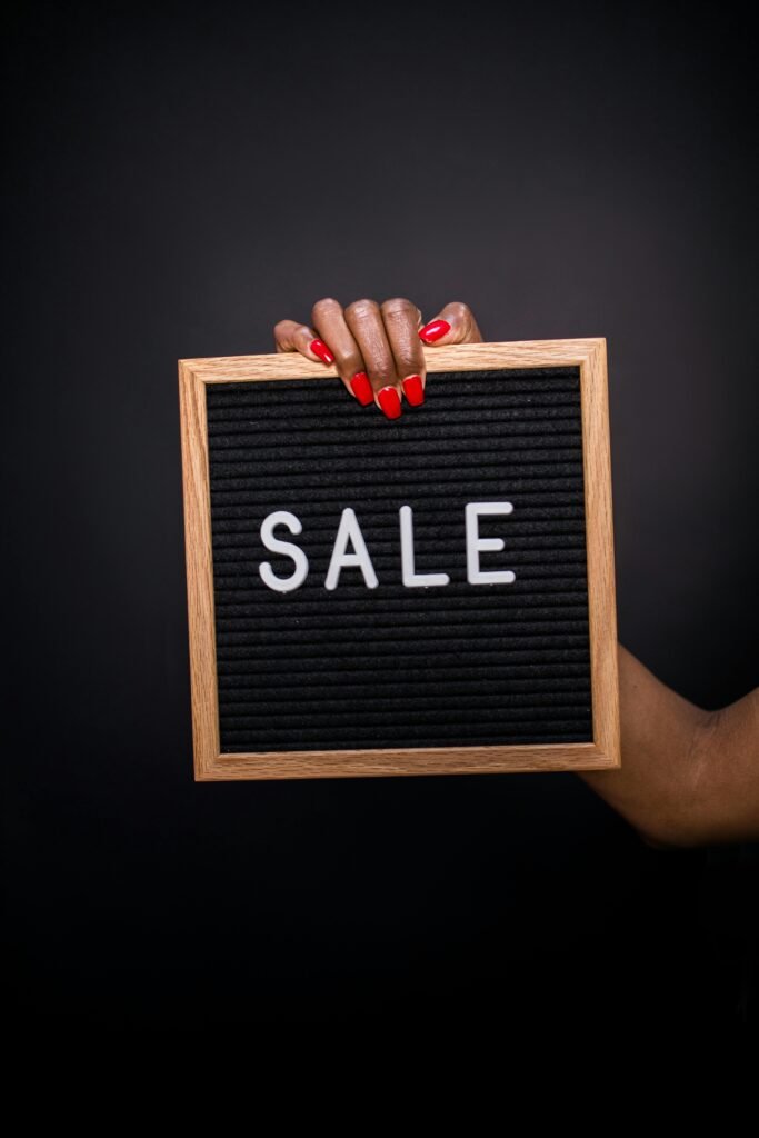 Close-up of a hand with red nails holding a SALE sign on black felt board.
